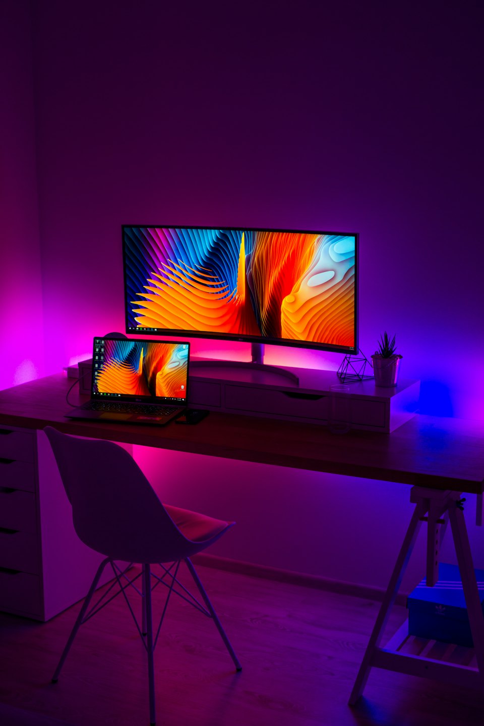 Ufficio moderno con monitor curvo e laptop che mostrano sfondi colorati.